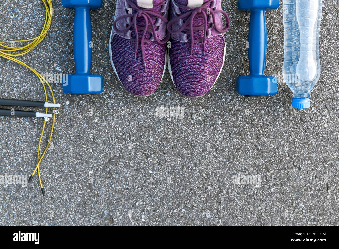 Motiviert zum Training. Zwei blaue dumpbells und Seil springen liegen in der Nähe von Purple Sport Schuhe. Eine Flasche Wasser in der Nähe liegen. Fitness als Hobby Stockfoto