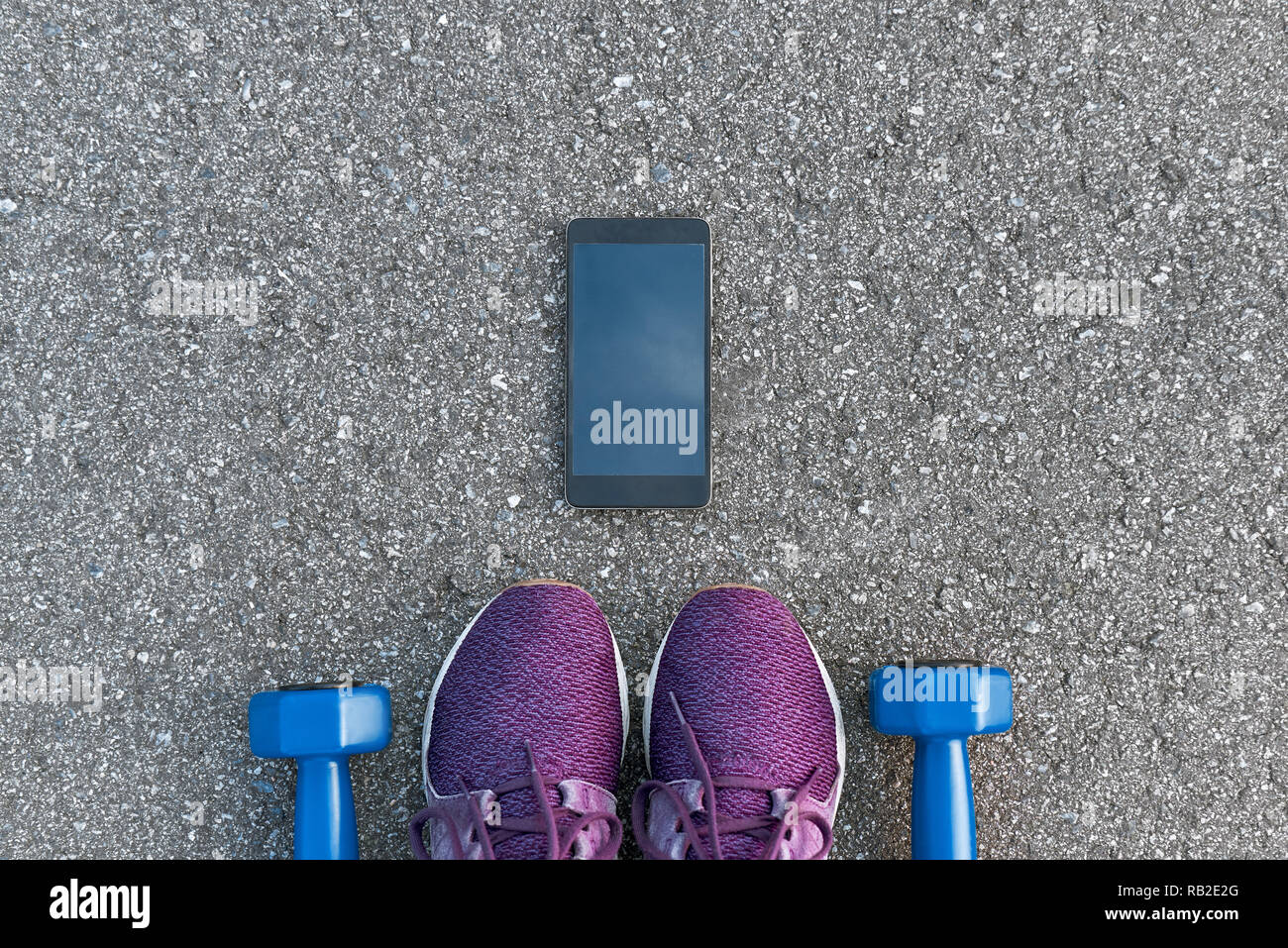 Smart sport Gadgets. Foto von dumpbells und lila Turnschuhe am Asphalt Hintergrund abgeschnitten. Sport motivation mobile Apps Stockfoto