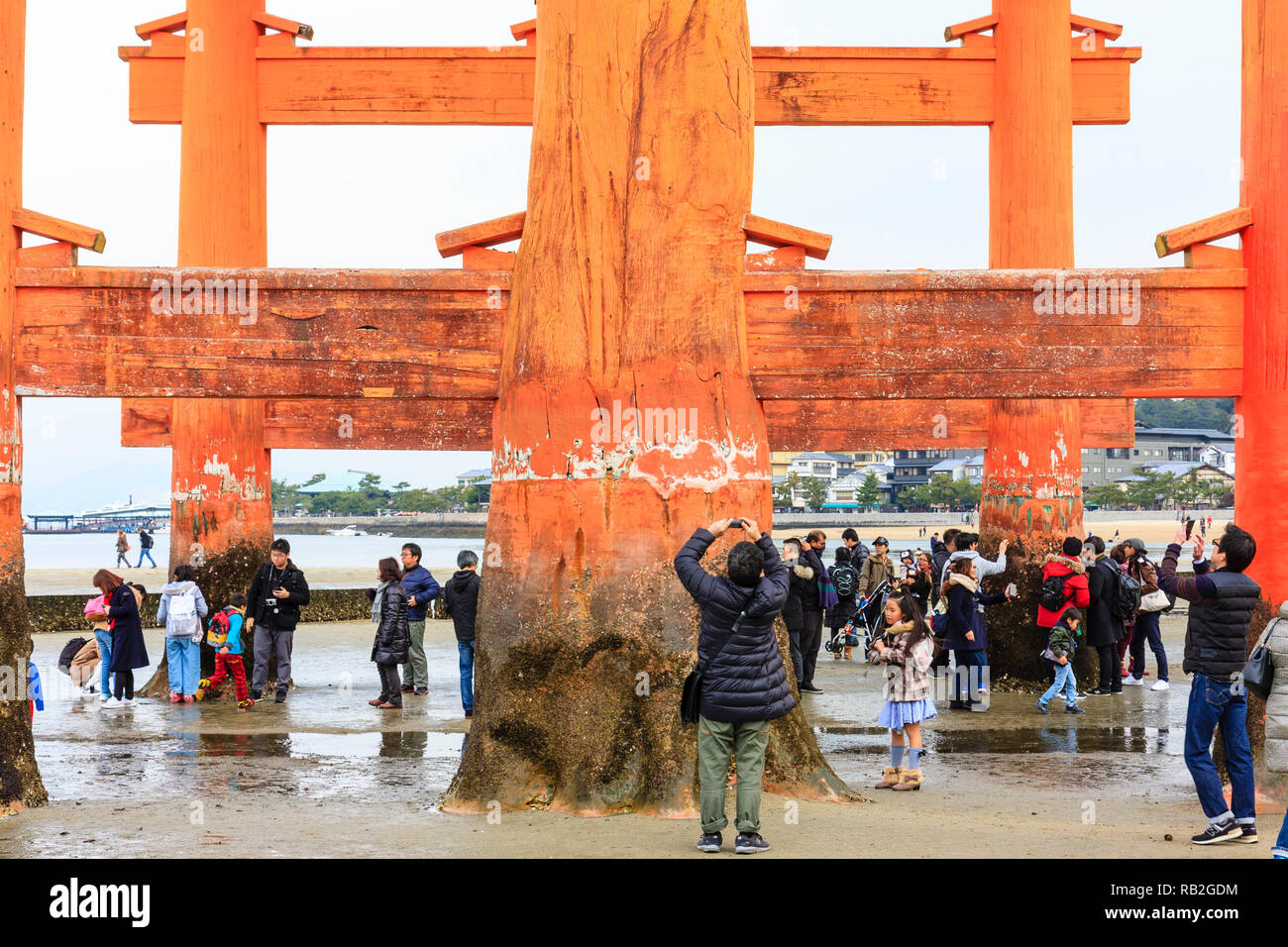 Japan. Die großen Torii an der Itsukushima Shinto Schrein auf der Insel Miyajima bei Ebbe mit Massen von Menschen rund um die drei Säulen an einem Ende. Stockfoto