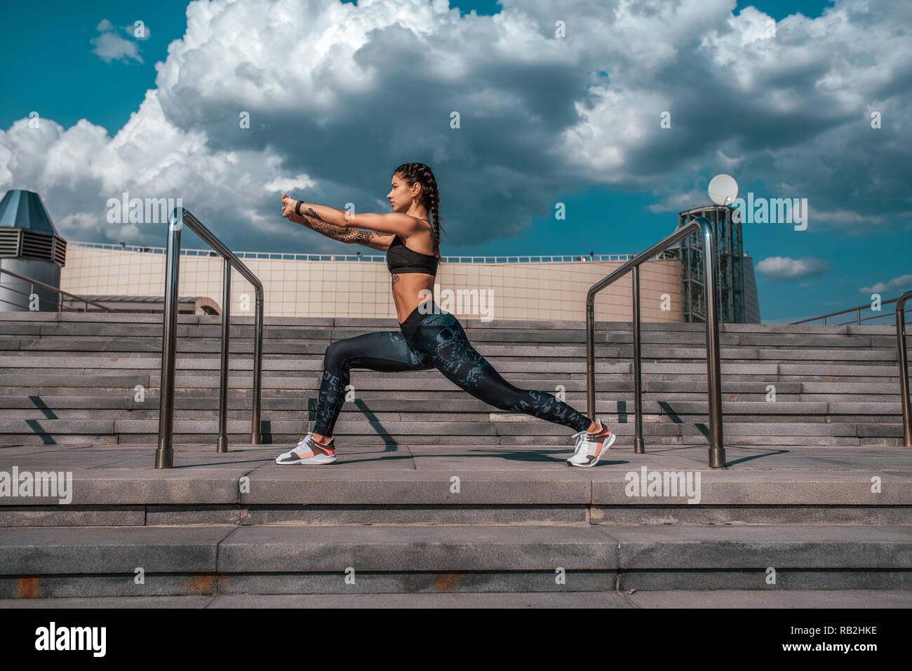 Das Mädchen mit Tätowierungen in Sportkleidung funktioniert ein Warm-up vor dem Turnen. Yoga. Vor dem Hintergrund der Treppen, im Sommer in der Stadt. Sport und gesunde Lebensweise. Stockfoto