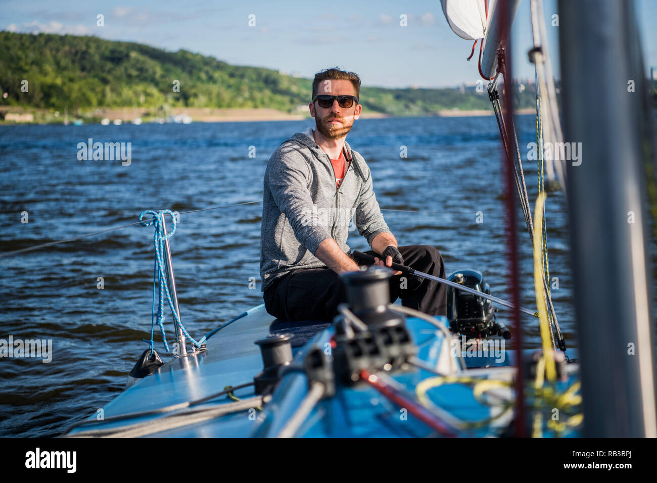 Ein Mann mit Sonnenbrille und legere Kleidung, als er ein kleines Beiboot rund um einen See oder Fluss Laufwerke Stockfoto