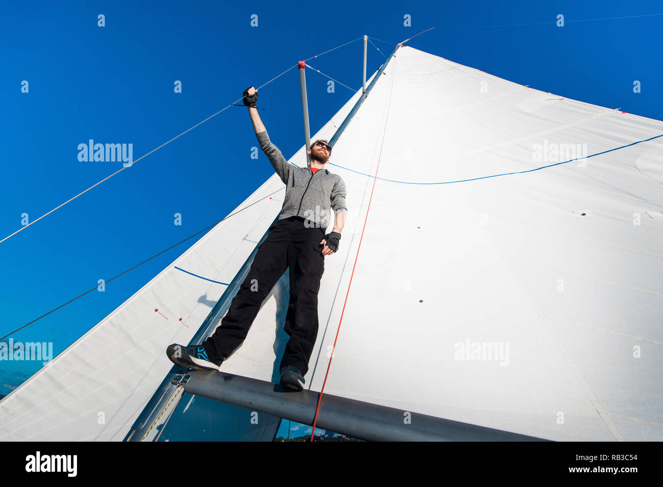 Schöne und selbstbewusste junge Mann steht auf Yachtcharter board und im Meer durch die Brille schauen. Er liegt am Rande der Yacht. Guy Holding segeln Seil in der Hand. Junge Mann ist glücklich und friedlich. Stockfoto
