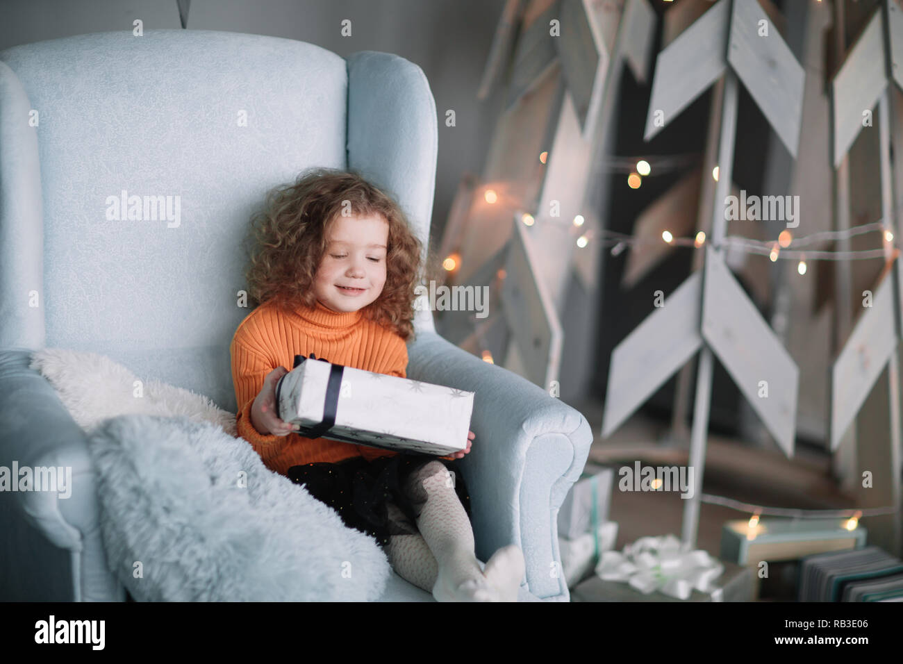 Kleines Mädchen mit einem Geschenk zu Weihnachten in einem bequemen Sessel sitzen Stockfoto
