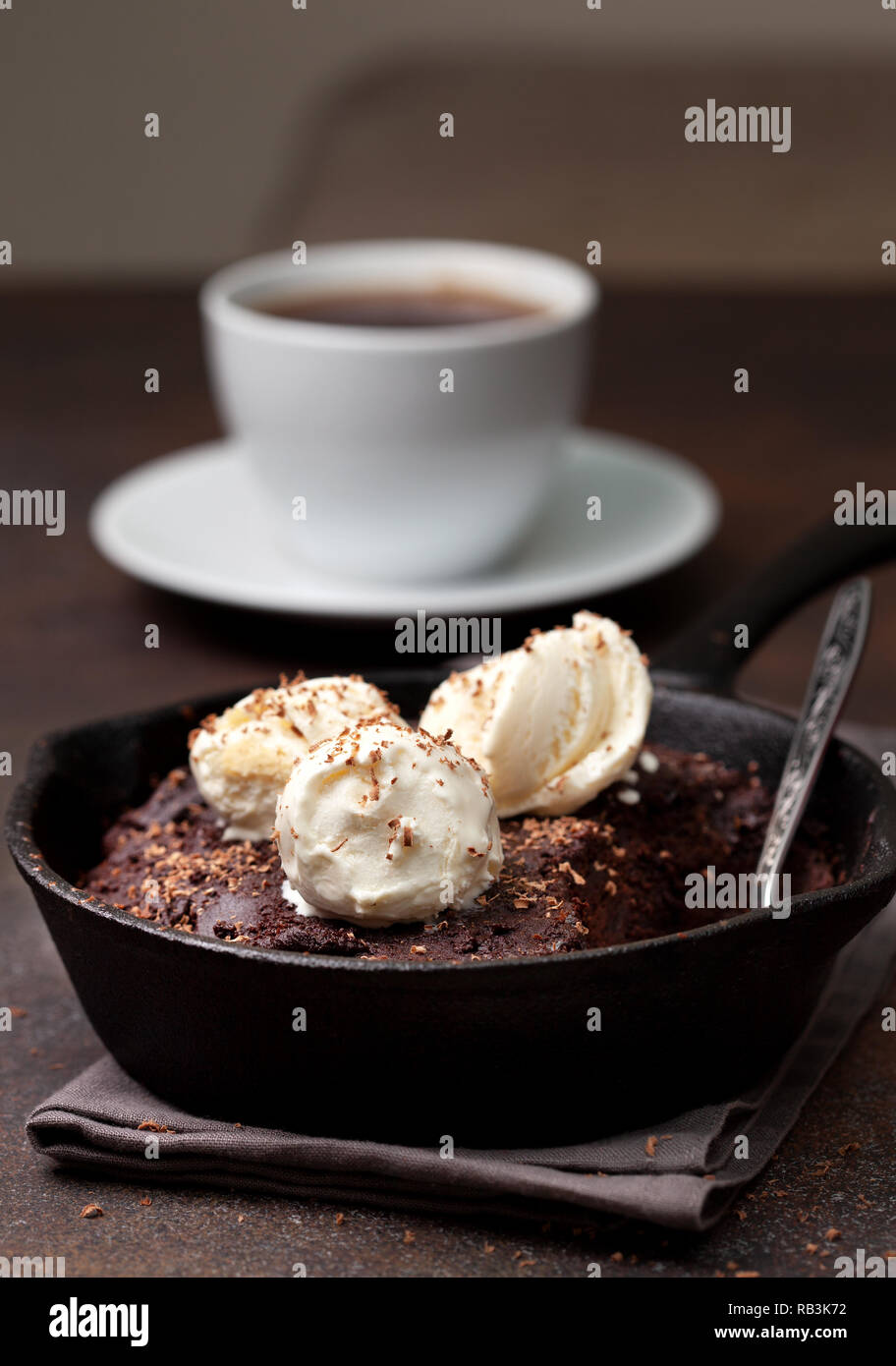 Brownies mit Vanilleeis in einer Pfanne, eine Tasse Kaffee auf braunem Hintergrund Stockfoto