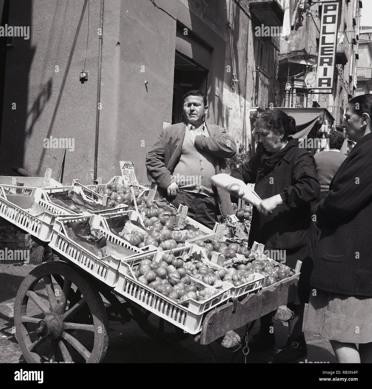1950er Jahre, eine Dame kaufen Gemüse aus Portable ist eine neapolitanische Frau Markt außerhalb Stall in einer Seitenstraße, Neapel, Italien Stockfoto