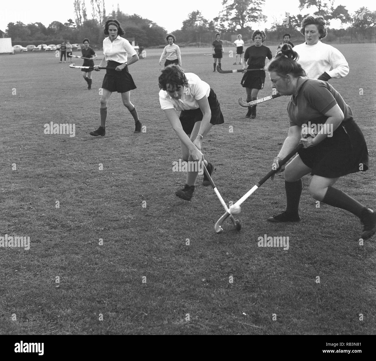 1960er Jahre, Mädchen und Damen draußen spielen ein Spiel der konkurrierenden Feld Hockey, England, Großbritannien Stockfoto