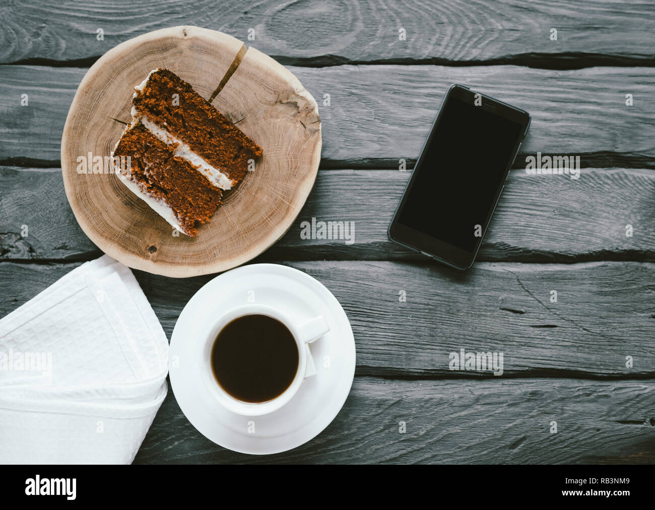 Stück hausgemachte Kekse Kuchen und Kaffee schwarz auf schwarzem Holz- Tabelle. Smartphone auf einem Tisch mit Essen. Köstliches Frühstück mit einer beschäftigten Person. Stockfoto