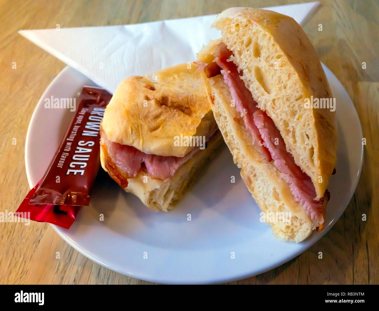 Ein Frühstück, Snacks, Gebutterte eine weiche, weiße Brötchen mit Schinken und mit sachets Brauner Soße und Tomatenketchup gefüllt Stockfoto