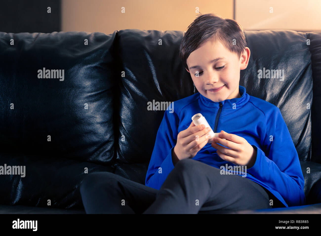 Acht Jahre alten Jungen tragen sportliche Kleidung Holding ein Asthma Inhalator sitzen auf einem Sofa. Konzepte: Gesundheit, Krankheit, Doping Stockfoto