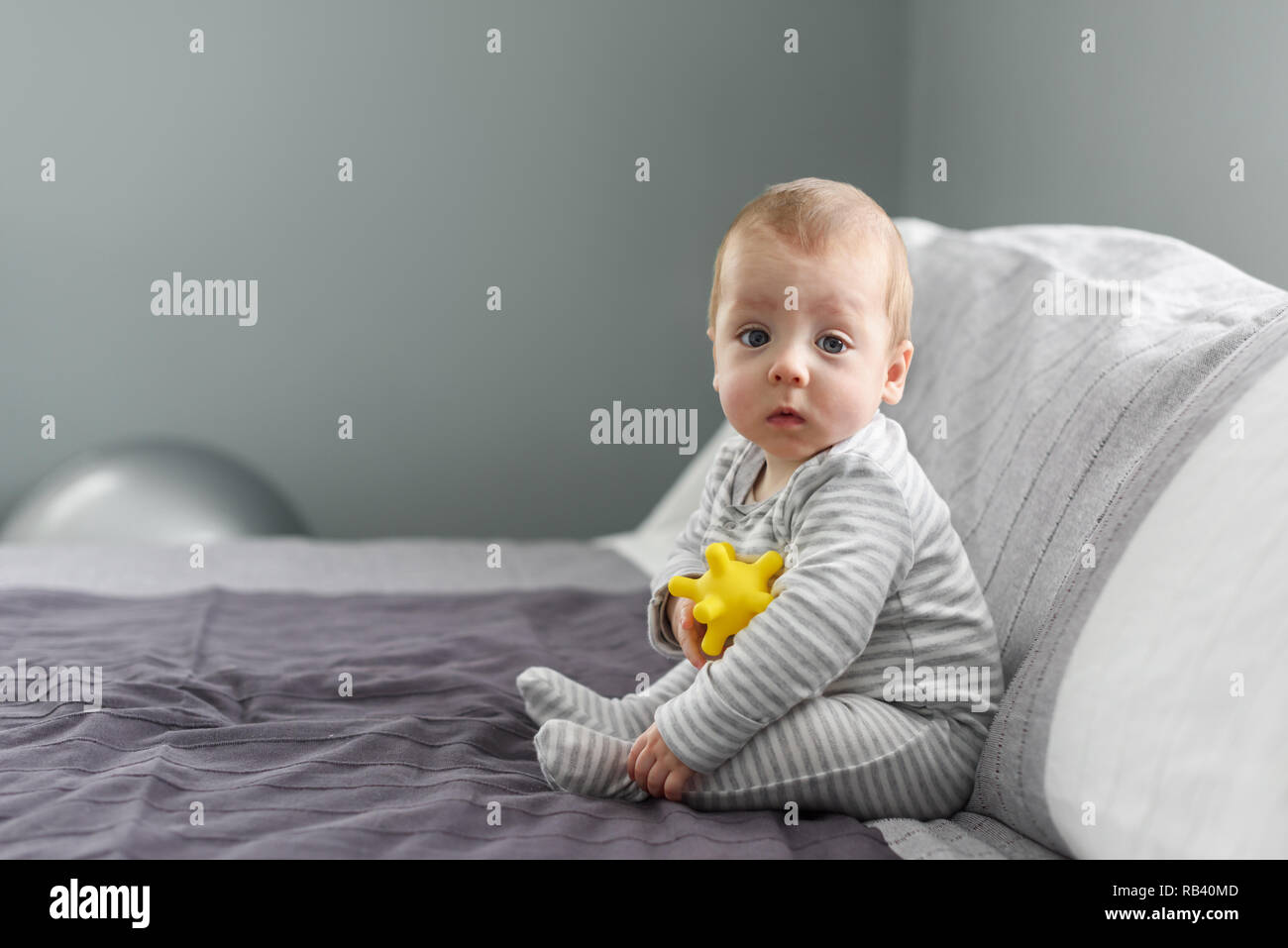 Sitzung Baby auf grauem Teppich mit gelben Ball Spielzeug. Mutterschaft und neues Leben Konzept Stockfoto