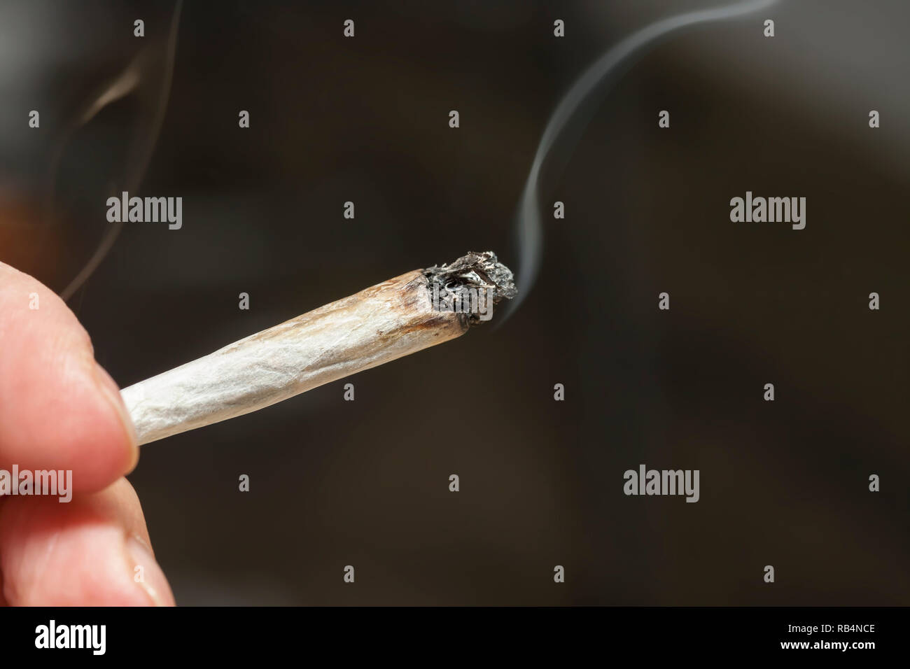 Nahaufnahme einer Hand, die eine beleuchtete Marihuana Joint gegen die dunkelgrauen Hintergrund Stockfoto