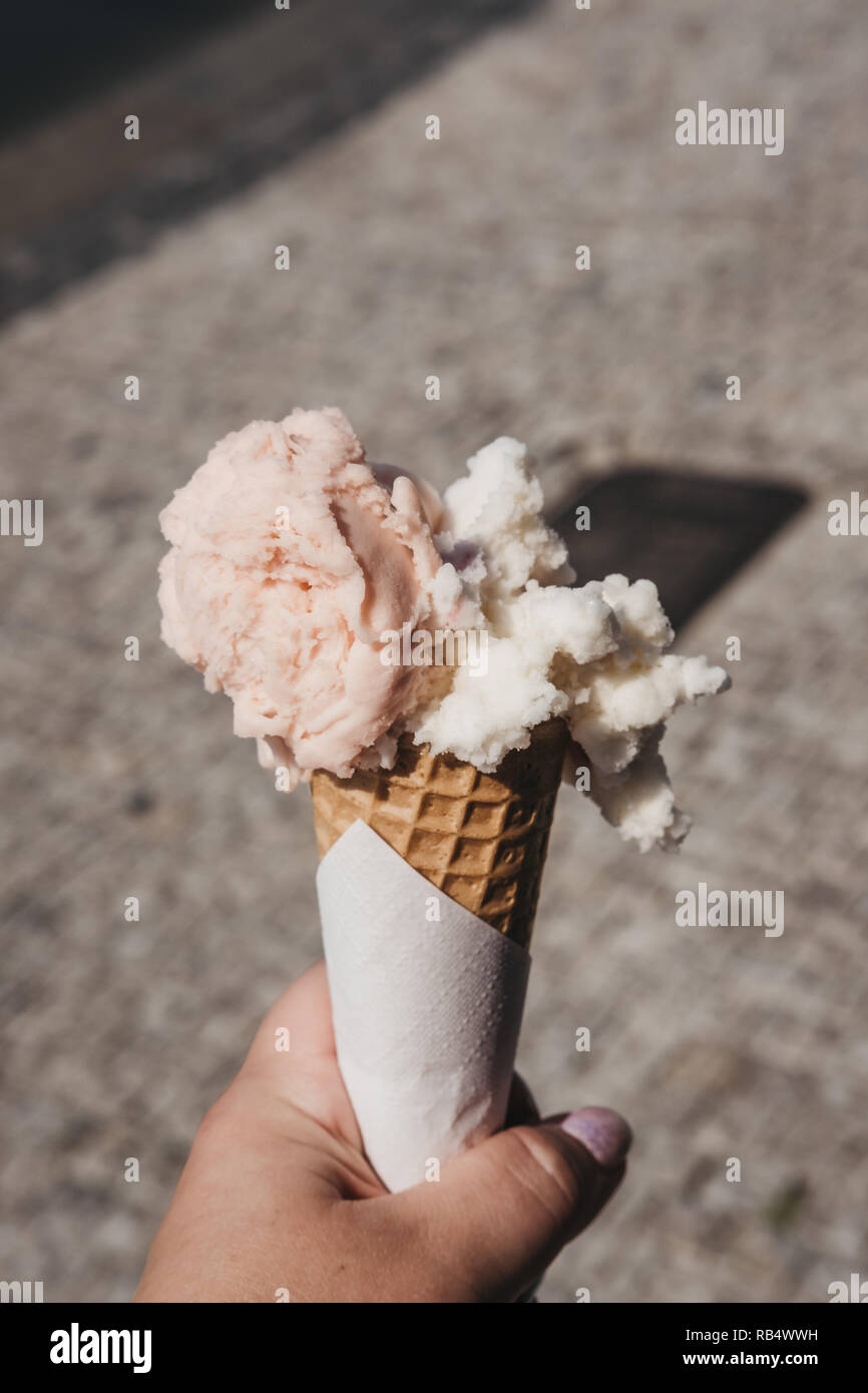 Bunte Eis in einem Wafer Kegel in der Frau in der Hand gehalten, verschwommenes Stadt im Hintergrund. Stockfoto