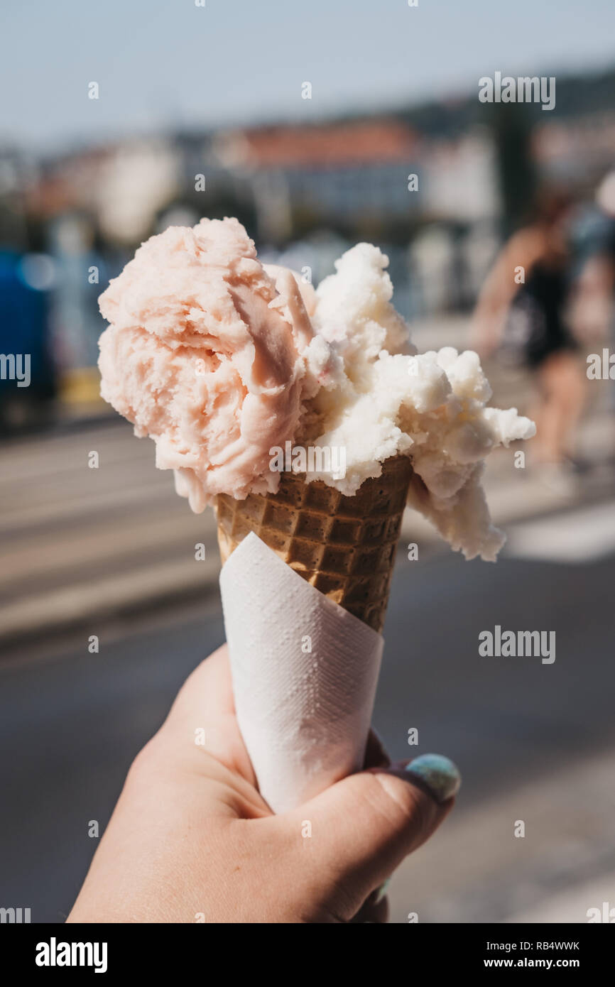 Bunte Eis in einem Wafer Kegel in der Frau in der Hand gehalten, verschwommenes Stadt im Hintergrund. Stockfoto