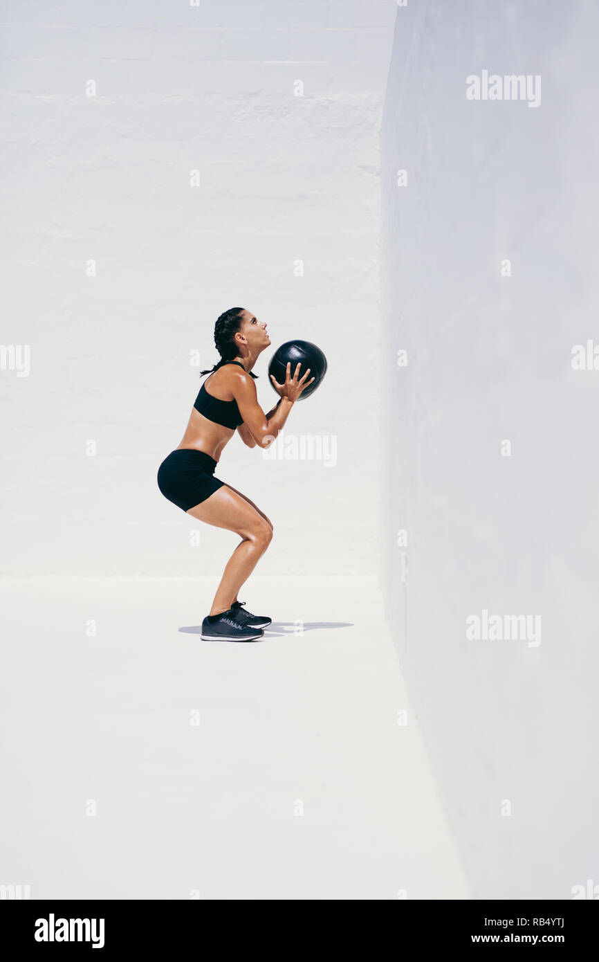 Weibliche Athleten dabei hockt Halte einen Medizinball. Seitenansicht einer Frau in fitness Verschleiß tun Workout mit einem medizinball. Stockfoto