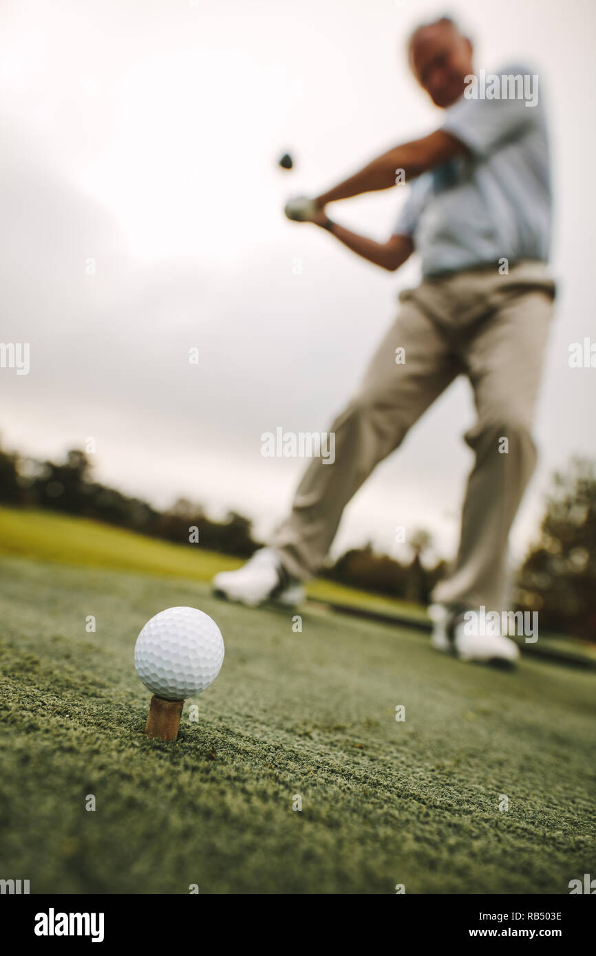 Golf Ball am T-Stück mit männlichen Spieler üben einen Schuß an die Strecke fahren. Fokus auf Golf Ball auf das T-Stück mit dem Golfspieler eine Aufnahme. Stockfoto