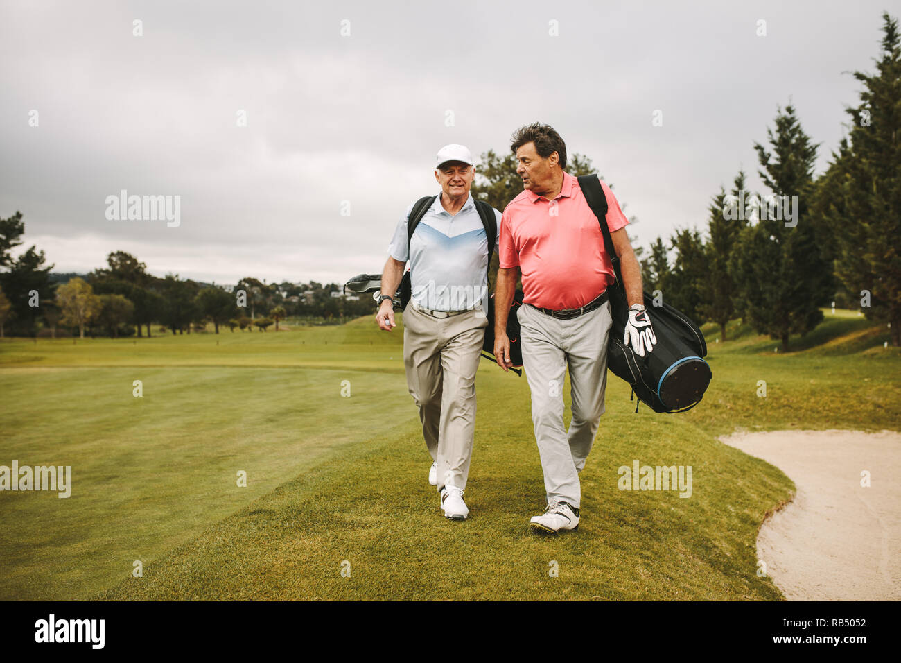 Zwei Freunde gehen durch den Rasen mit Golfausrüstung und sprechen. Ältere Golf Spieler zusammen zu Fuß auf den Golfplatz. Stockfoto
