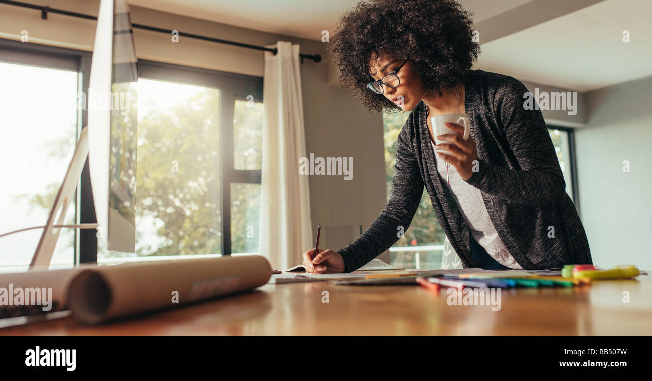 Architekten arbeiten an Pläne und Grundrisse. Frau mit Tasse Kaffee Notizen in ein Buch zu Hause Büro. Stockfoto