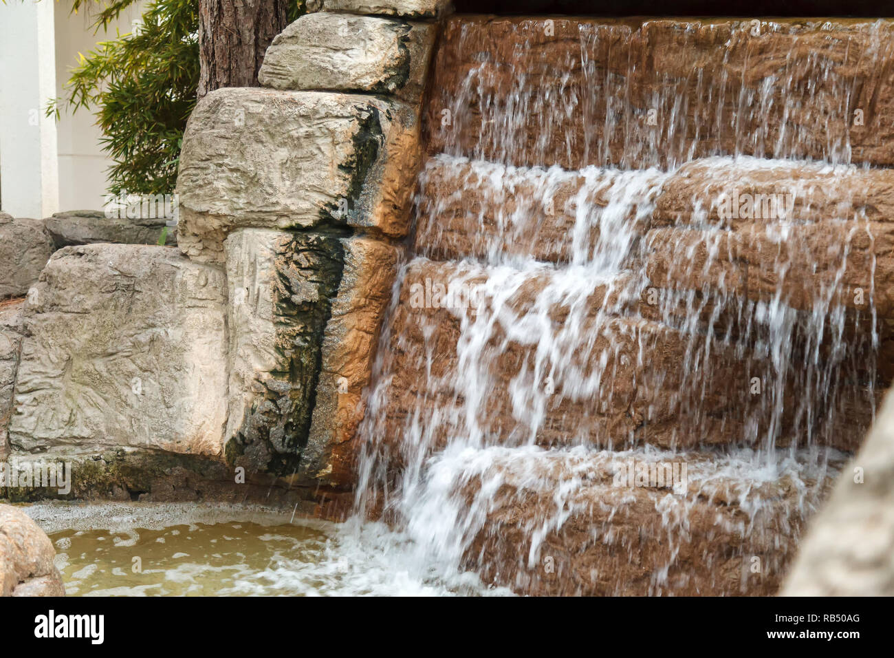 Kühle klare Wasser fließt durch eine Kaskade von künstlicher Wasserfall aus Steinen. Wasser von oben und bildet Schaum bei fällt. Stockfoto