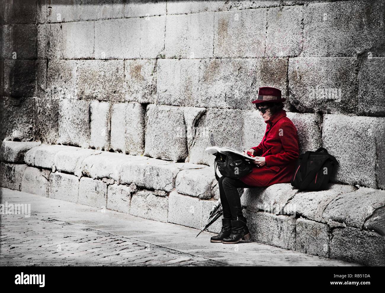 Dame in Rot, eine Dame in einem roten Mantel bekleidet sitzt auf einer Steinbank lesen. Stockfoto