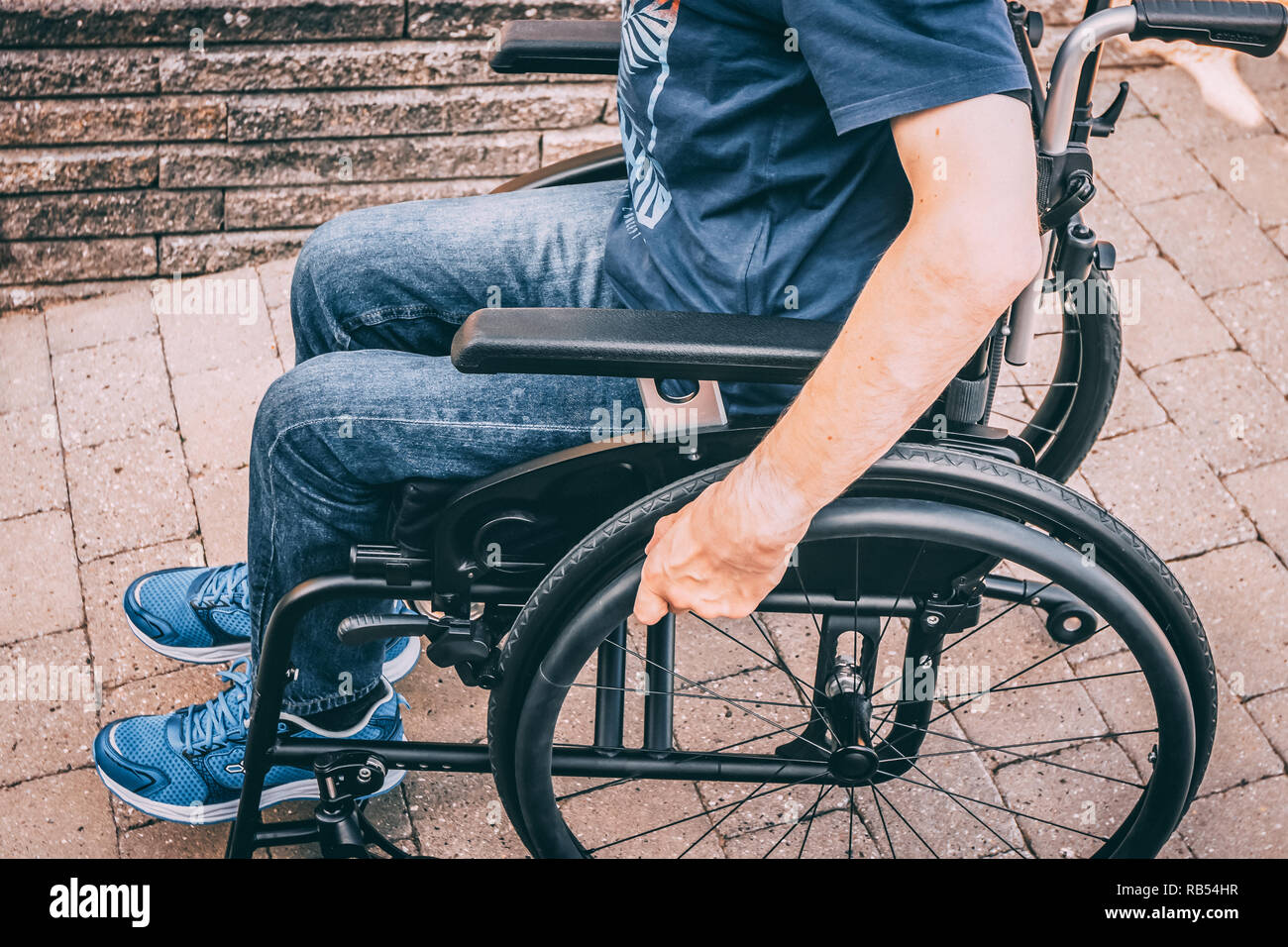 Mann mit dystonie im Rollstuhl, Hände auf Rad auf dem Weg nach unten Stockfoto