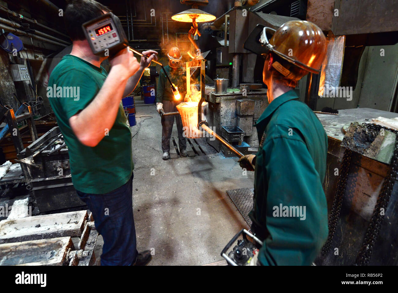 Arbeitnehmer in einer Gießerei gießen ein Werkstück aus Metall - Sicherheit bei der Arbeit und Teamarbeit Stockfoto