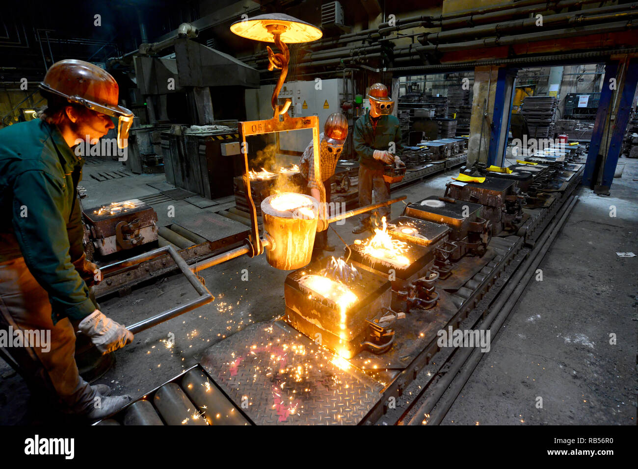 Arbeitnehmer in einer Gießerei gießen ein Werkstück aus Metall - Sicherheit bei der Arbeit und Teamarbeit Stockfoto