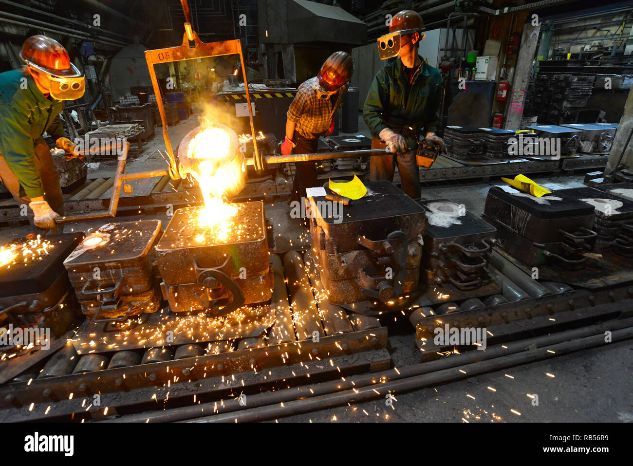Arbeitnehmer in einer Gießerei gießen ein Werkstück aus Metall - Sicherheit bei der Arbeit und Teamarbeit Stockfoto
