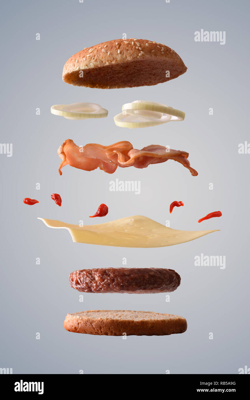 Classic Beef Burger mit Speck, Zwiebeln und Käse floating mit Zutaten, die in Teile zerbrochen auf grauen Farbverlauf isoliert Hintergrund. Vorderansicht. Verti Stockfoto