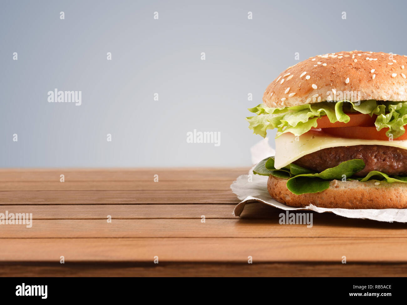 Classic Beef Burger mit Käse, Tomaten und Salat auf Holztisch mit grauem Hintergrund. Vorderansicht. Horizontale Komposition. Stockfoto