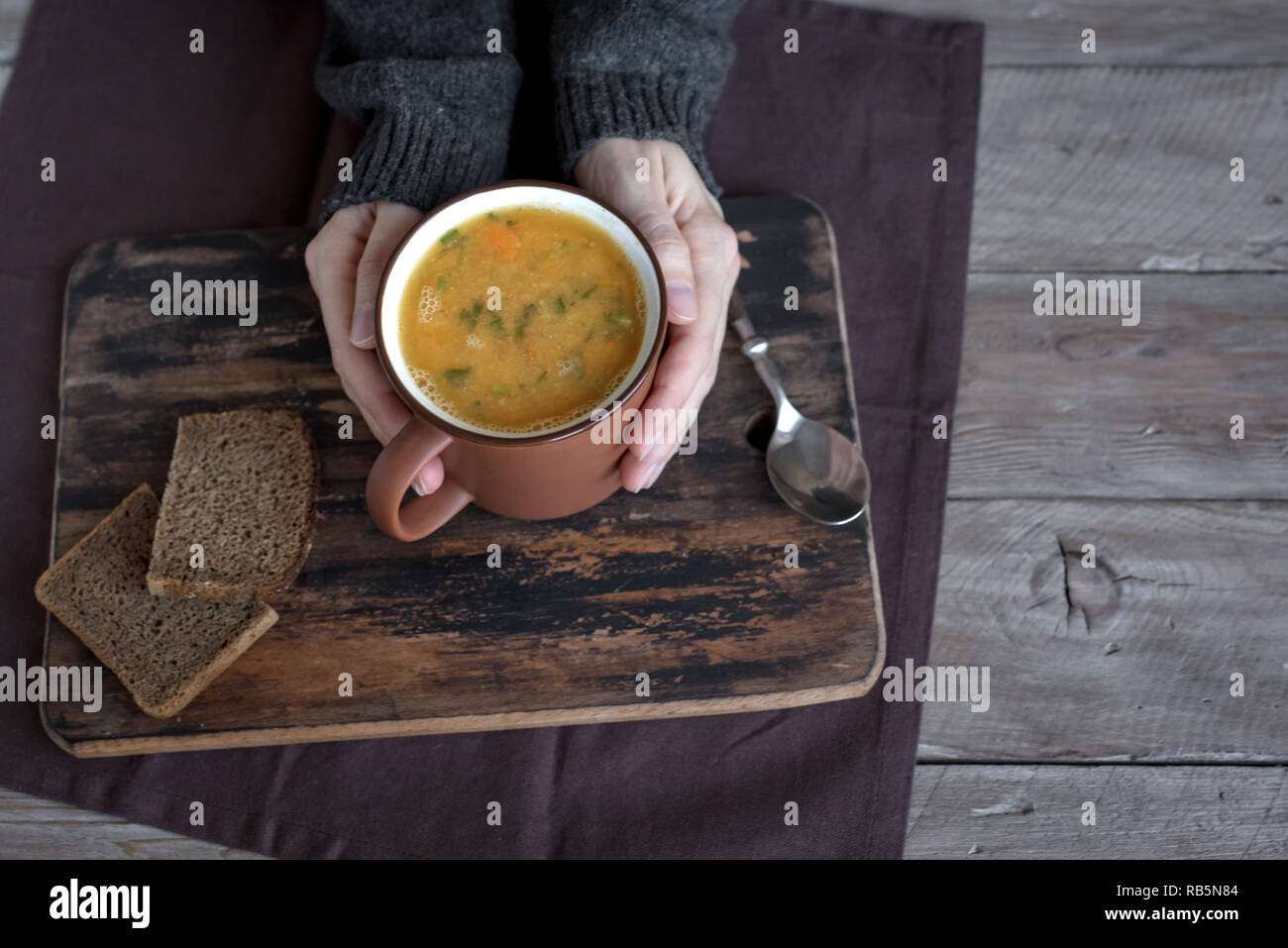 Frau Hände halten Tasse Gemüsesuppe auf Holzuntergrund - gesunde Winter vegetarisches Essen, gemütliche wärmende Suppe. Stockfoto