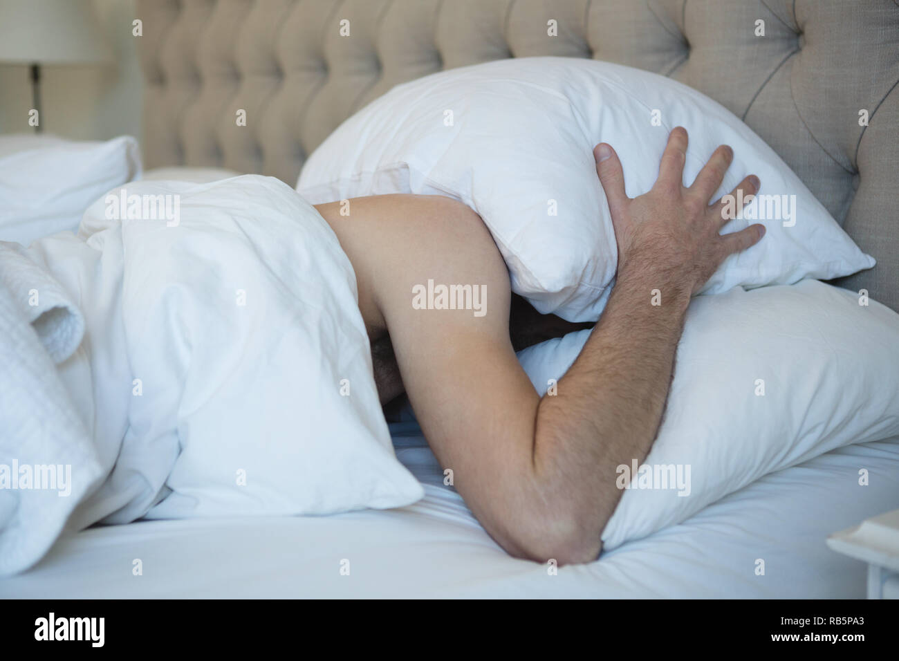 Mann mit Kissen bedeckte sein Gesicht beim schlafen im Schlafzimmer Stockfoto