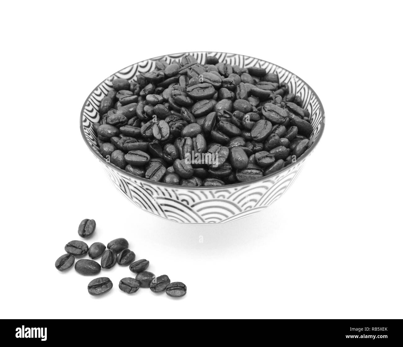 Dunkel geröstete Kaffeebohnen in einem gemusterten Keramik Schüssel, einige Neben, auf einem weißen Hintergrund - monochrom Verarbeitung verschüttet Stockfoto
