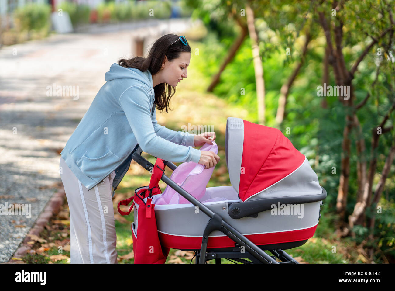 Eine junge Mutter schaut sich das Baby in einem Kinderwagen für einen Spaziergang im Park Stockfoto