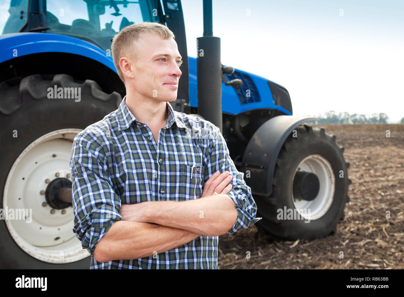 Junger attraktiver Mann in der Nähe von einem Traktor. Konzept der Landwirtschaft und Feld arbeitet. Stockfoto