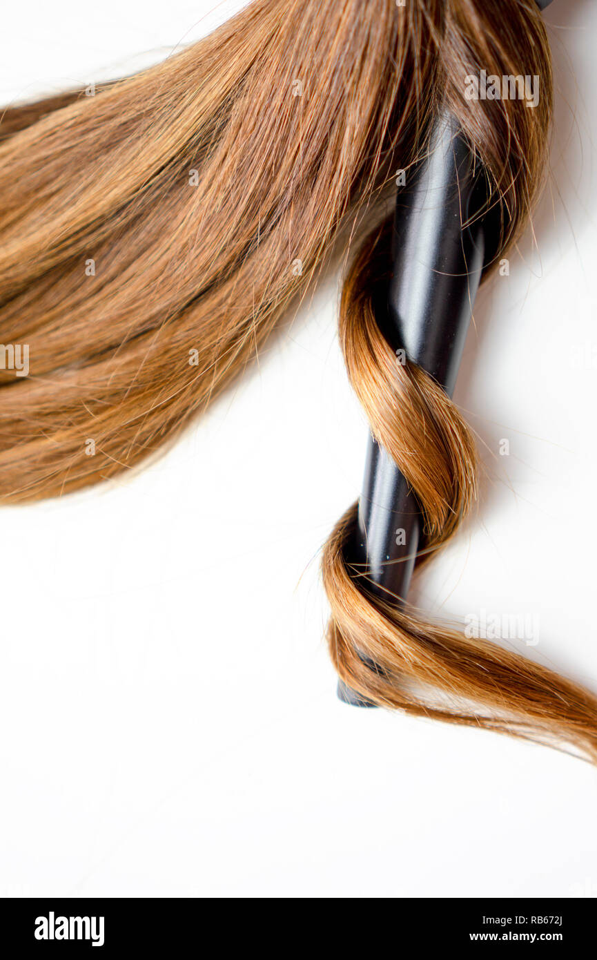 Braun glänzendes Haar auf weißem Hintergrund isoliert mit Curling winken Bügeleisen Stockfoto