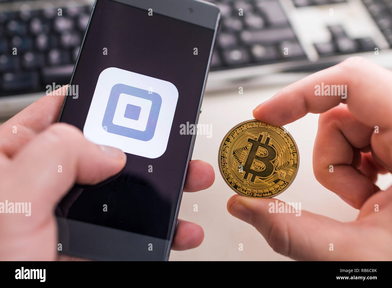 Slowenien - Januar 8, 2019: Mann hält Bitcoin Münze und in der anderen Hand Smartphone mit quadratischen Anwendung. Stockfoto