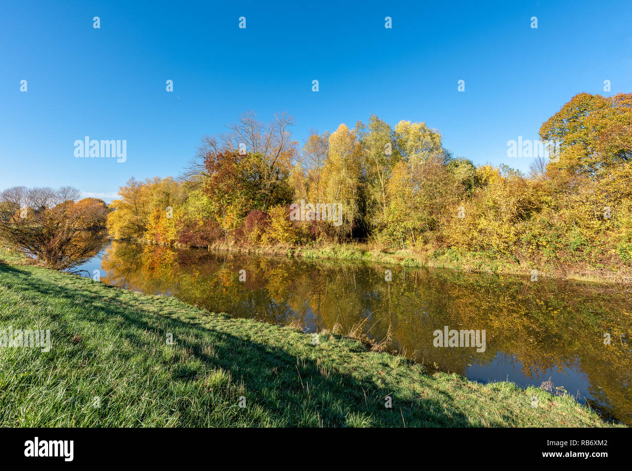 Farbe outdoor Herbst Natur Bild einer ländlichen herbstlichen Fluss Szene mit blauer Himmel, bunte Bäume auf dem Wasser auf einem hellen, sonnigen Tag widerspiegelt Stockfoto