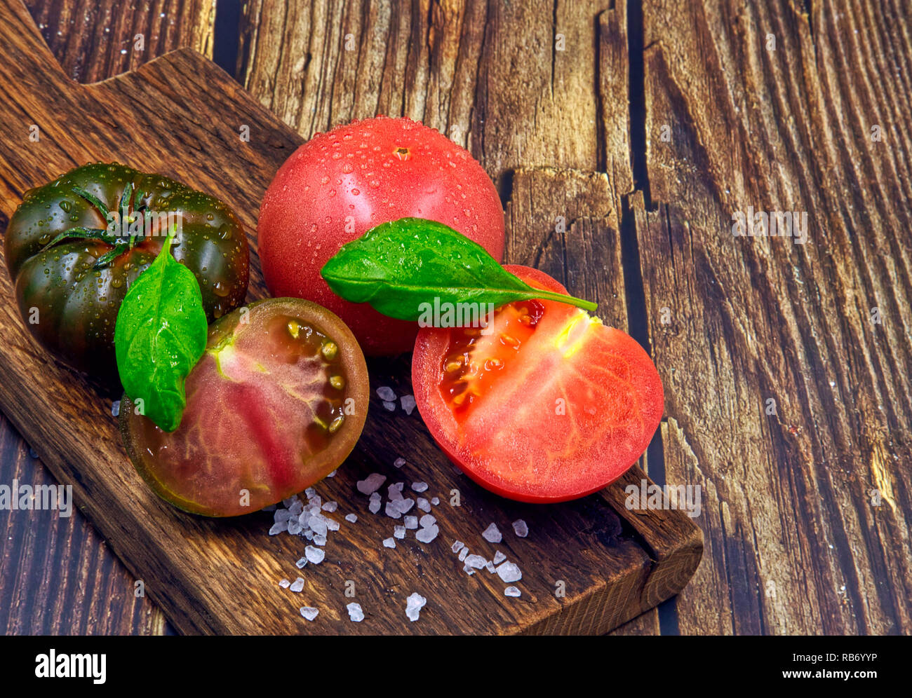 Flache Ansicht von oben auf frischen schwarzen und roten Tomaten und deren Schnitt Hälften mit deutlich sichtbaren Details, auf einem alten hölzernen Schneidebrett. Vintage Style. Stockfoto