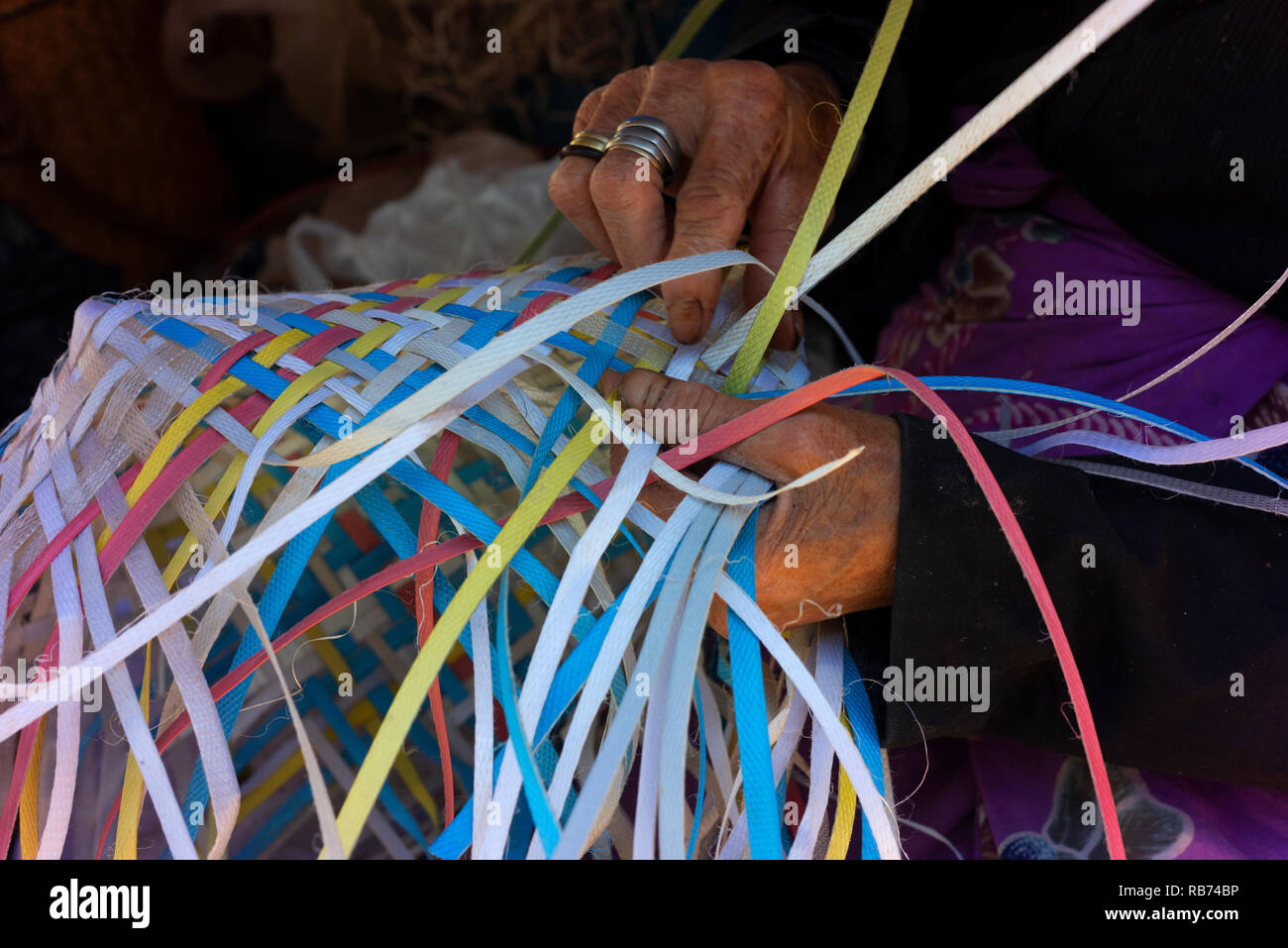 Eine ältere Frau spinnt einen Korb von zerrissen Streifen aus Kunststoff/Hessische gemacht. Stockfoto