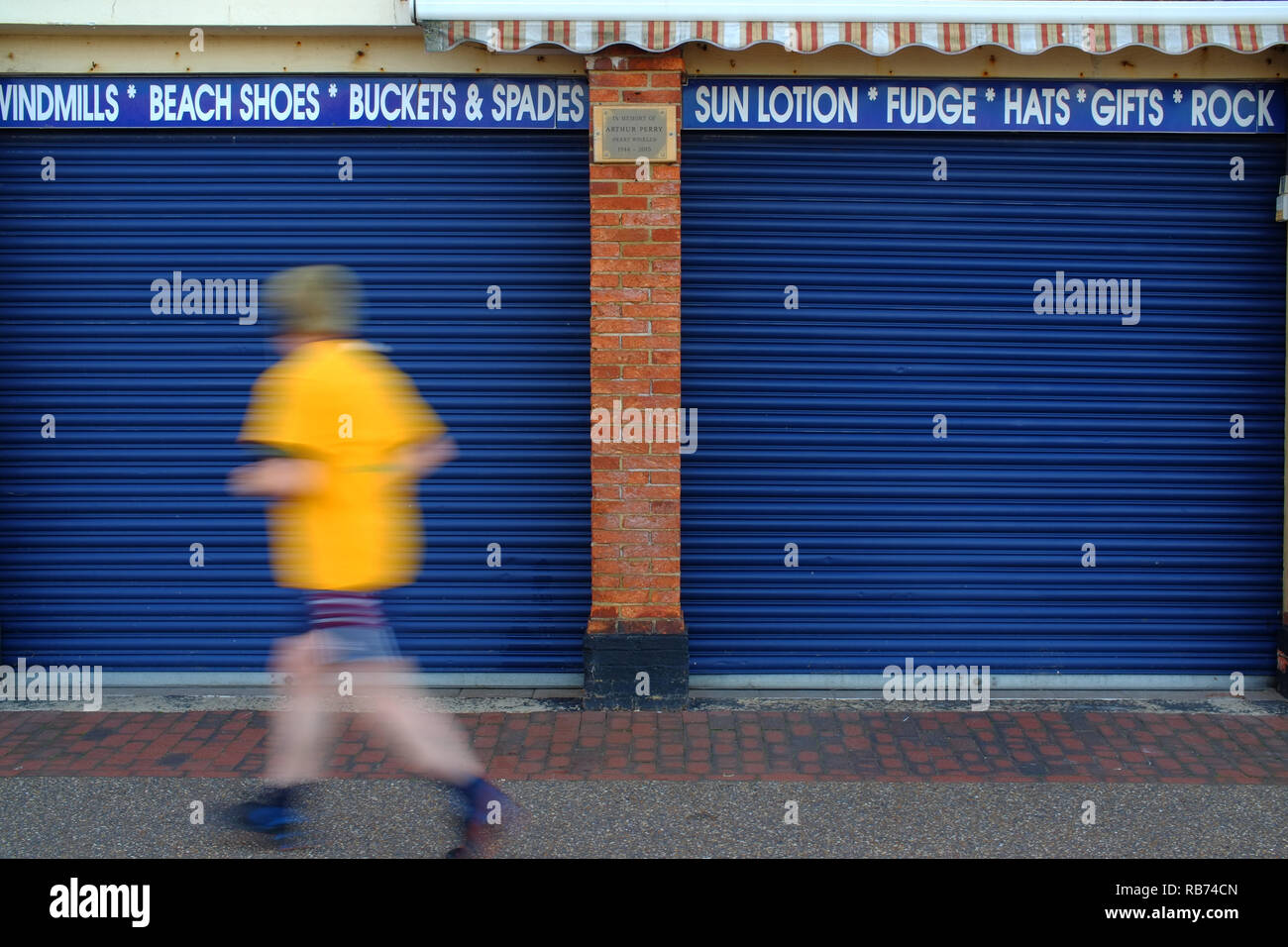 Mann in einem gelben Top jogging Vergangenheit ein Shuttered seaside Shop. Stockfoto