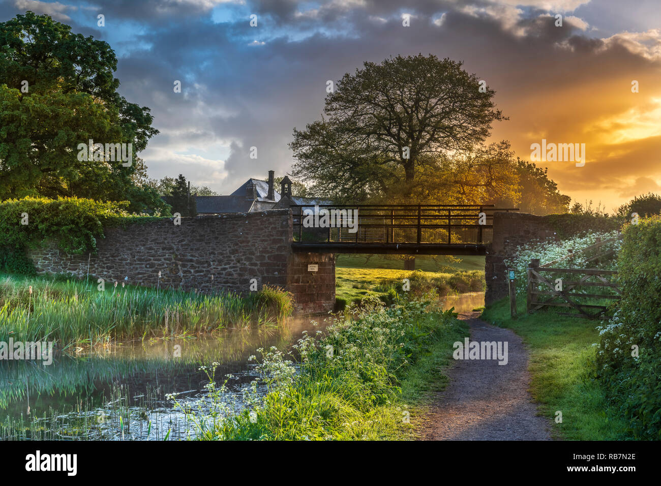 UK Wetter - nach einer Nacht des schweren Duschen, erhebt sich die Sonne hinter Ayshford Brige auf der Great Western Canal in der Nähe von Samford Peverell in Devon. Stockfoto