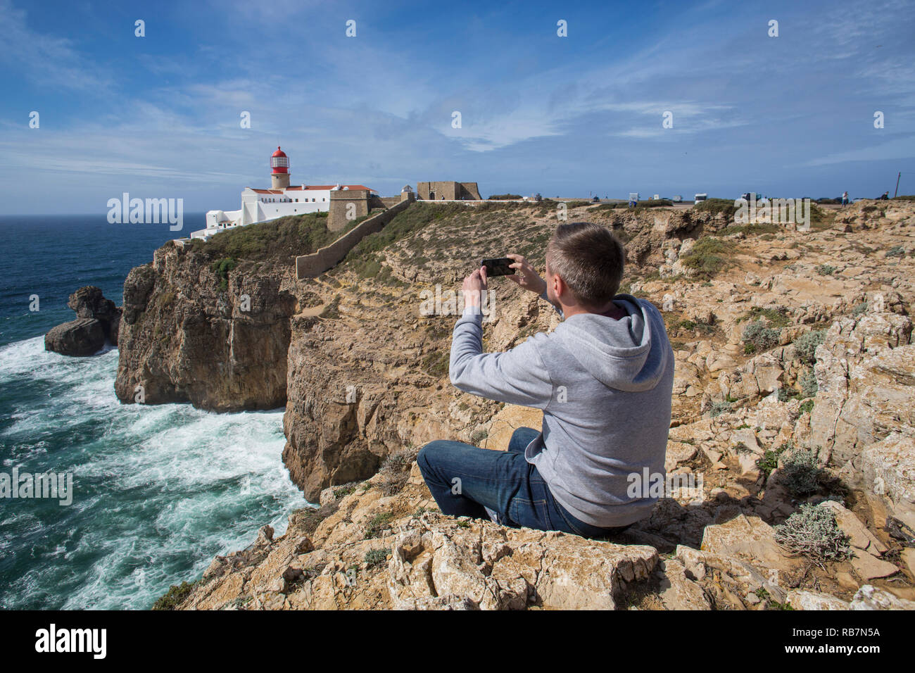 Mann sitzt auf den Fels und unter Foto von Sagres Leuchtturm am Kap St. Vincent. Stockfoto