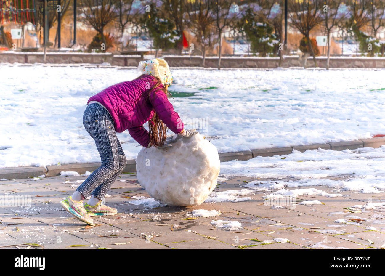 Nicht identifizierte Mädchen rollt eine große und schwere Schneeball einen Schneemann in einem Spiel im Winter zu bauen Stockfoto