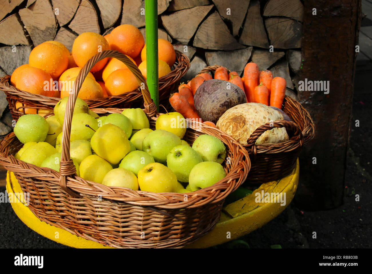 Frische Äpfel, Orangen, Karotten und Rüben in Weidenkörbe in der Nähe der Wand von Rundholz. Gesunde Ernährung und Diät Konzept. Stockfoto