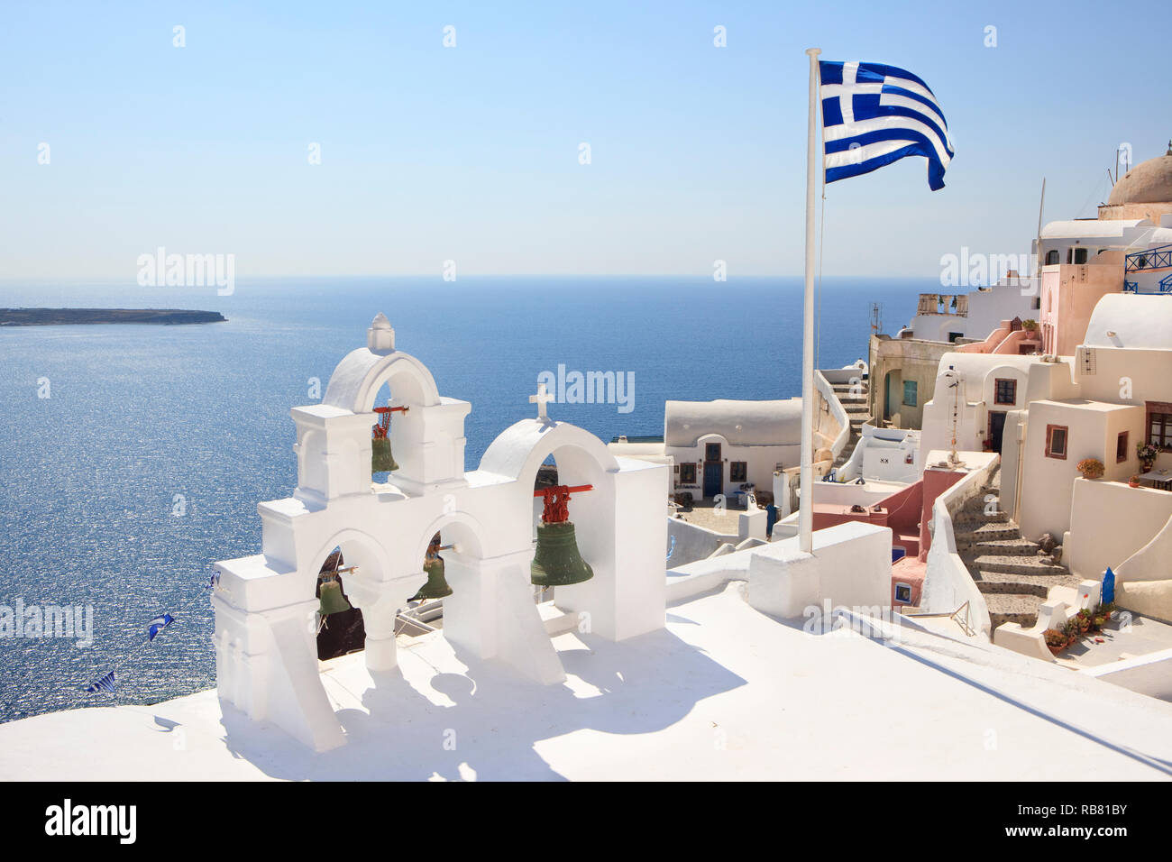 Stadt Oia auf Santorini (Kykladen). Blick auf Kirche mit Glocken auf dem Vulkan rim (Caldera). Griechische Flagge. Stockfoto