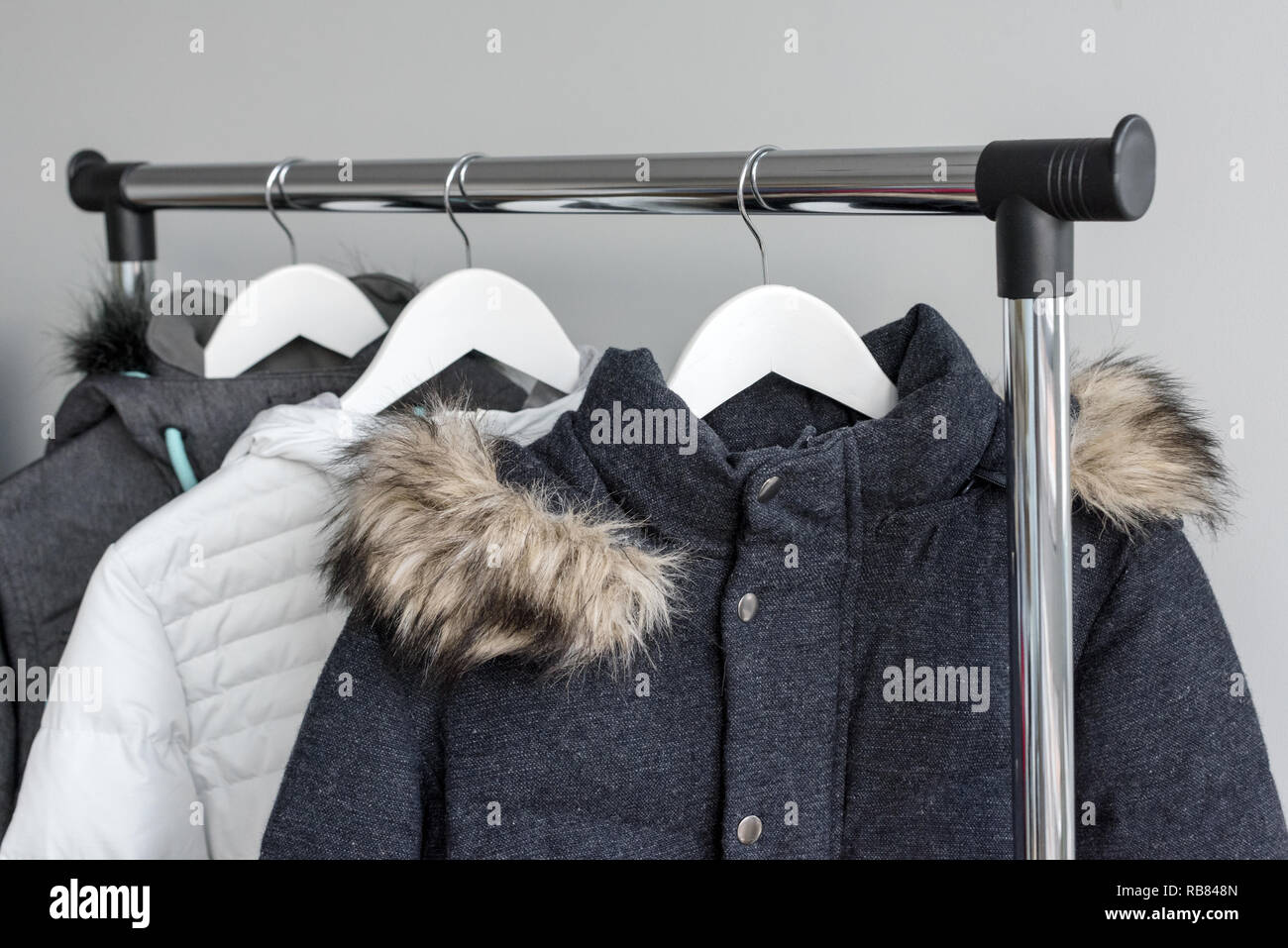 Hanger stand mit warmen Jacken. Winter Jacken mit Pelzkragen hängen auf weißem Holz Bügeln. Sammlung von winter Jacken im Shop. Winter Mode Hintergrund Stockfotografie
