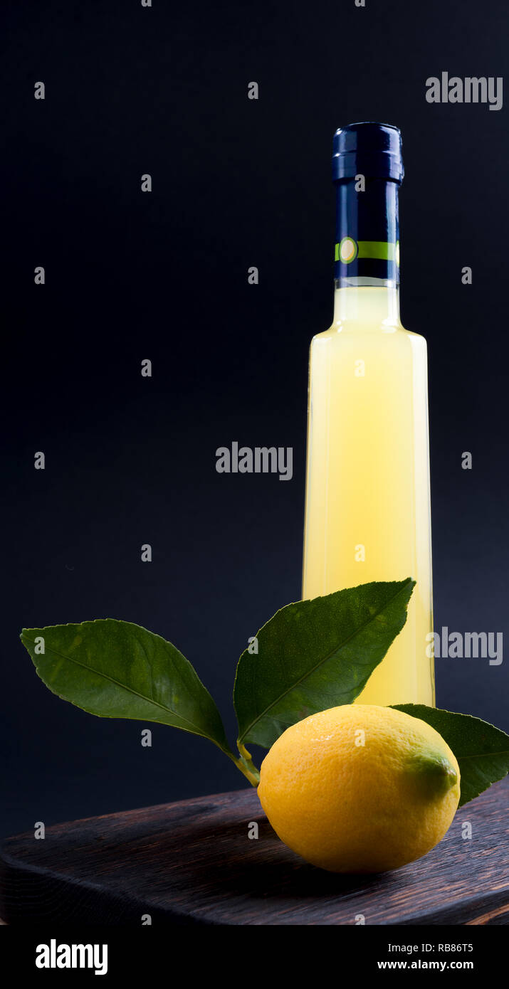 Lemoncello in einer Flasche auf einem schwarzen Hintergrund, traditionelle italienische Likör aus Zitronen. Alkohol gelb und frische Zitrone mit grünen Blättern. Für tex Platz Stockfoto