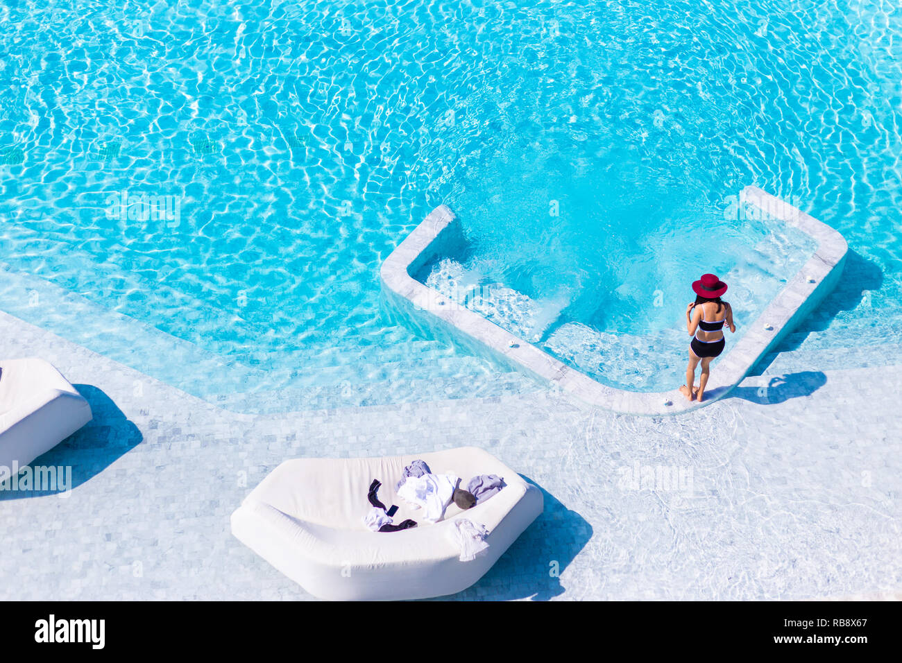 Junge Frau im schwarzen Badeanzug und Red Hat über in den Pool im Freien Whirlpool auf einem hellen, sonnigen Tag zu erhalten Stockfoto