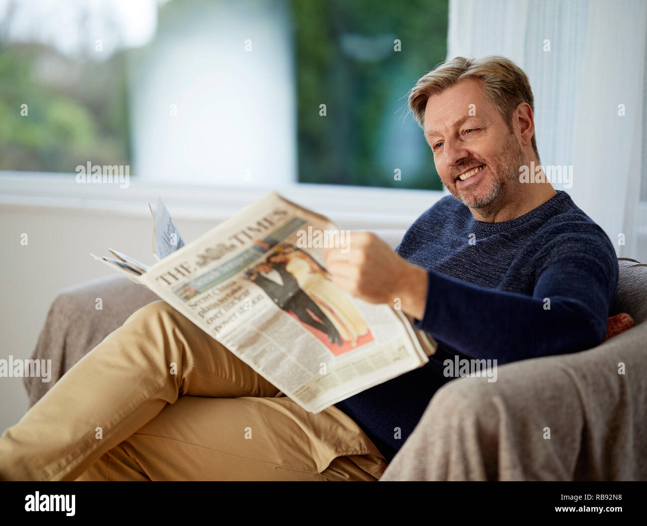 Mann entspannt auf einem Sofa lesen ein Papier Stockfoto