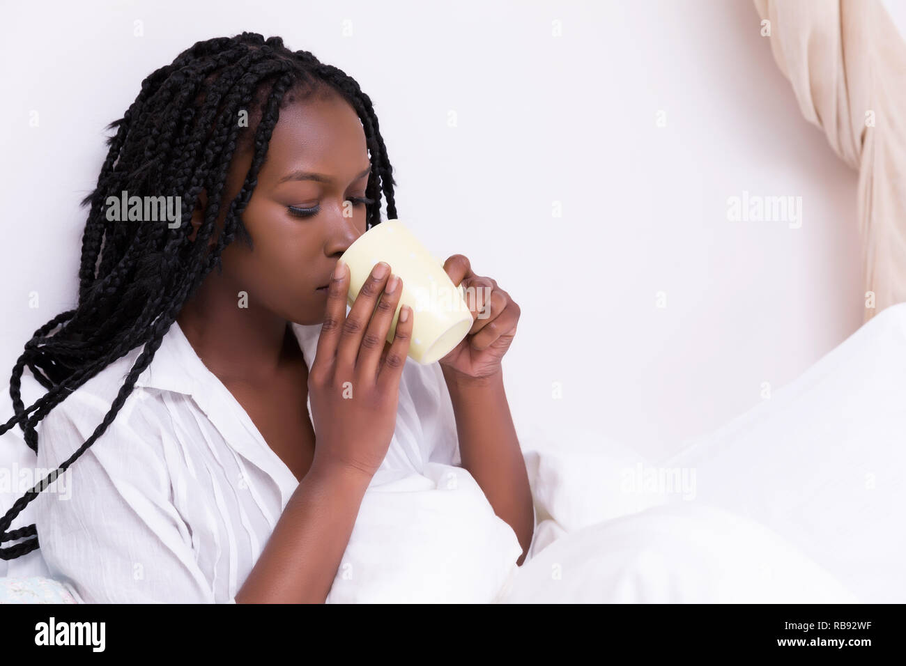 Schöne afrikanische Frau mit langen Zöpfen entspannen Sie sich auf ihrem Bett am Morgen Stockfoto